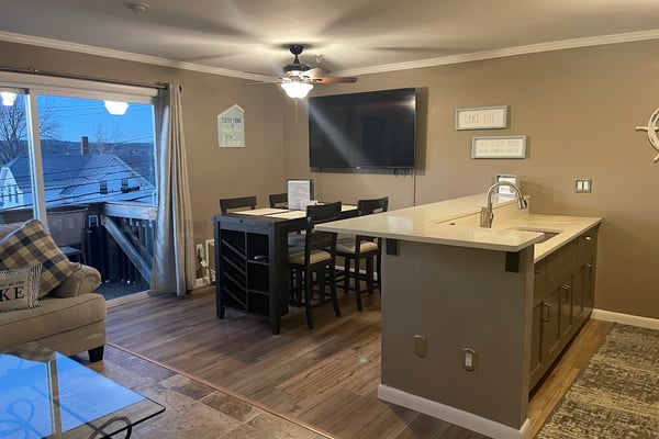 Open kitchen and bar area with wood cabinets, stone-faced island, bar seating, and dining table with ceiling fan