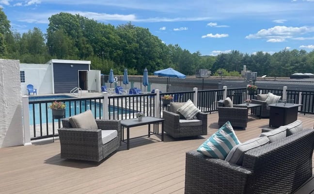 Outdoor pool deck with wicker lounge seating, firepits, and blue umbrellas at Condo Suites Lake Winnipesaukee